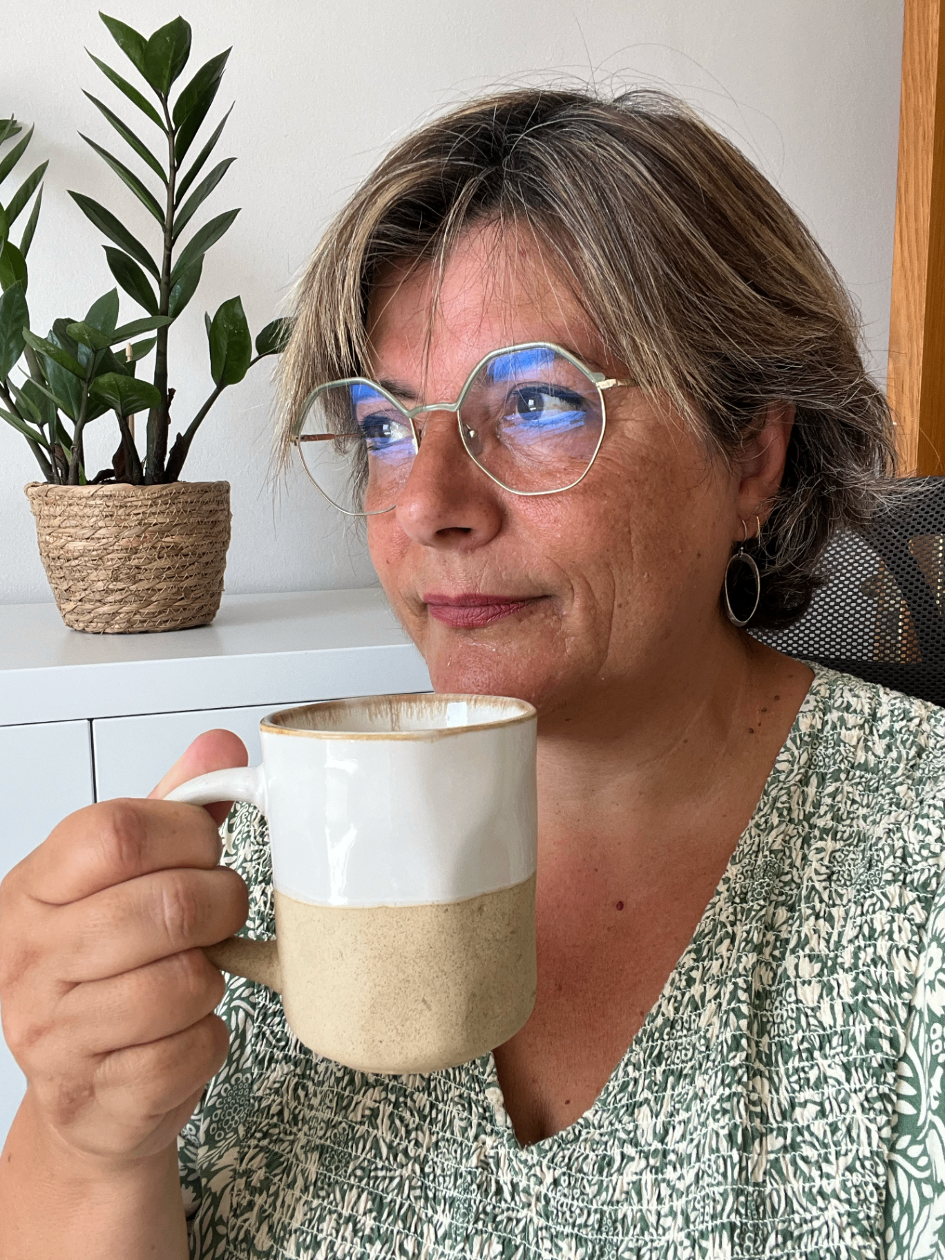Dona en un espai càlid sostenint una tassa al costat d'una finestra